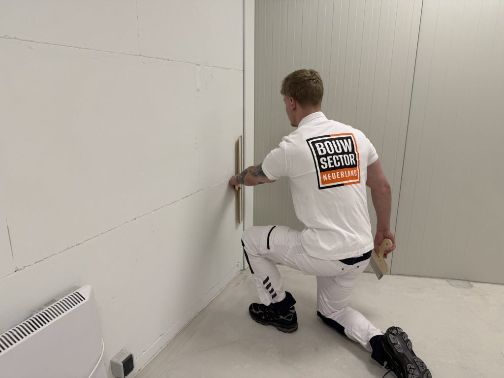 Stukadoor zit op een knie en trekt het onderste deel van een binnenwand vlak met een spaan